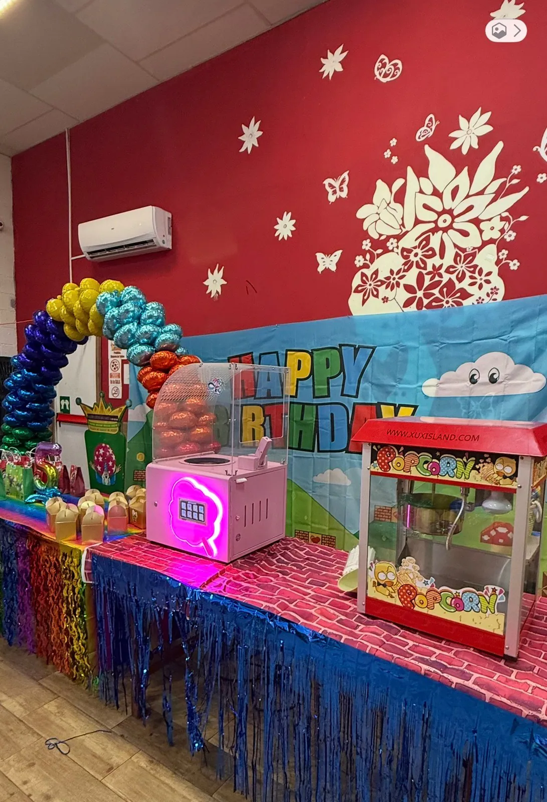 Mesa dulce de cumpleaños con máquina de algodón de azúcar y máquina de palomitas de Xuxisland, con arco de globos de colores